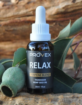 A bottle of Provex Relax Enhanced Hemp Seed Oil with a dropper, placed on a rock with green foliage in the background.